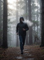 Model wearing black hooded anorak outdoors on a forest trail