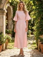 Woman wearing a pink cotton-linen ruffle midi dress with three-quarter sleeves in a sunlit garden courtyard