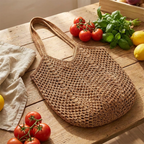 Crochet mesh knit tote bag with dual shoulder straps on a sunlit wooden market table