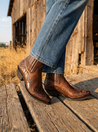 Embroidered western ankle boots worn outdoors on weathered wooden boards in warm afternoon light