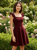 Woman wearing the claret fit-and-flare mini dress with ruffle straps in a garden