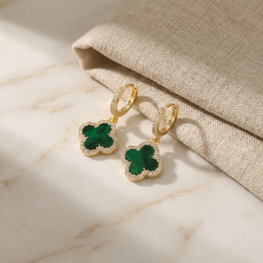Gold-tone four-leaf clover enamel earrings on a pale marble surface
