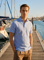 Man wearing a light blue linen short sleeve polo shirt on a harbour marina walkway