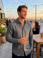 Man wearing a grey linen button-front summer shirt on a rooftop bar at evening