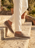 Taupe suede slip-on loafers worn with cream trousers on stone terrace steps