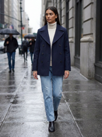 Woman wearing a navy double-breasted pea coat walking on a city sidewalk