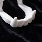 Close up of white vampire fangs costume teeth on black velvet