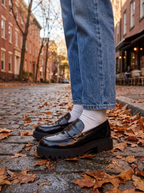 Black platform loafers with a chunky lug sole worn on an autumn city street
