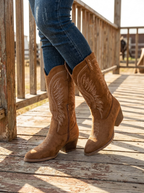 Tan western cowboy boots with a mid-calf shaft worn with jeans on a wooden porch